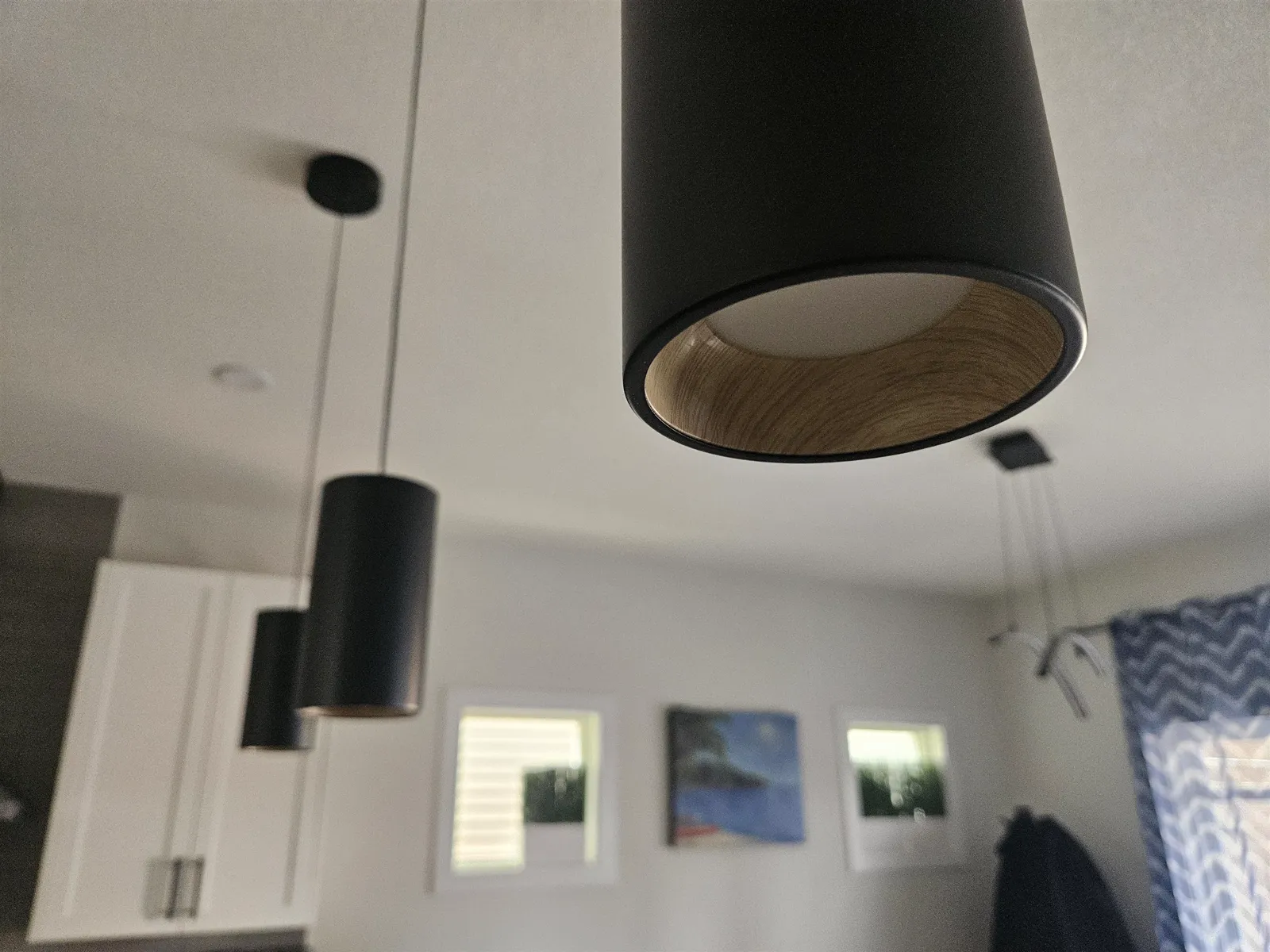 Black cylinder pendants with wood-grain interiors over a kitchen island